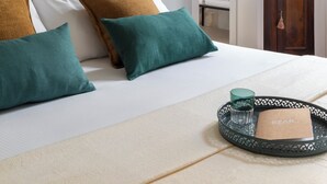 Un dormitorio ordenado con cama, almohadas, una bandeja con un vaso y un libro, y un armario de madera con flores.