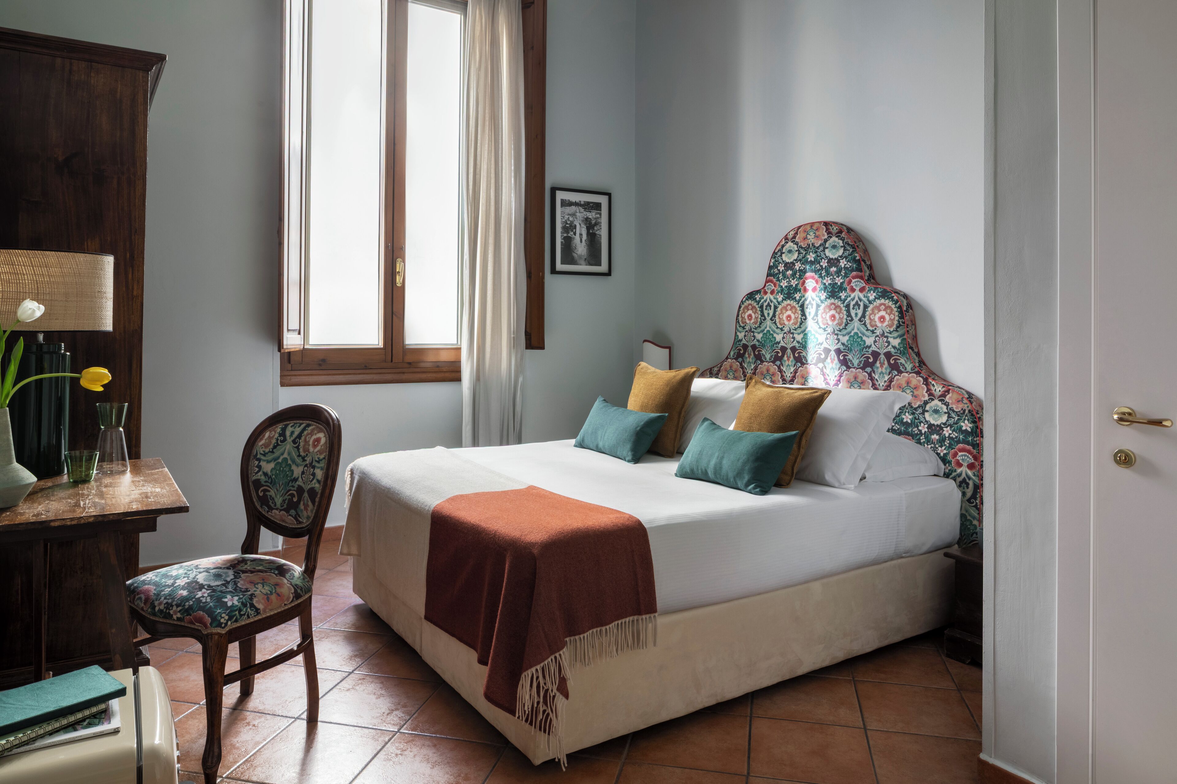 A bedroom with a bed, a chair, a desk, and a window.