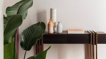 A minimalist room with a dark wooden console table, a white wall-mounted lamp, and large green plants.