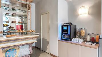 Un espace pour le petit-déjeuner à l’hôtel, doté d’un comptoir en marbre, d’une machine à café et de différents distributeurs de nourriture et de boissons.