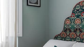 A neatly made bed with a white and red blanket, a teal pillow, and a framed picture on the wall.