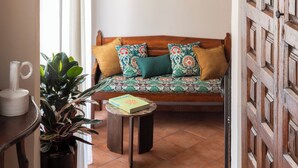 Un interior con un arco de ladrillo, una puerta de madera con diseño de cuadrícula, un sofá con cojines estampados, una pequeña mesa con un libro y una planta en maceta.
