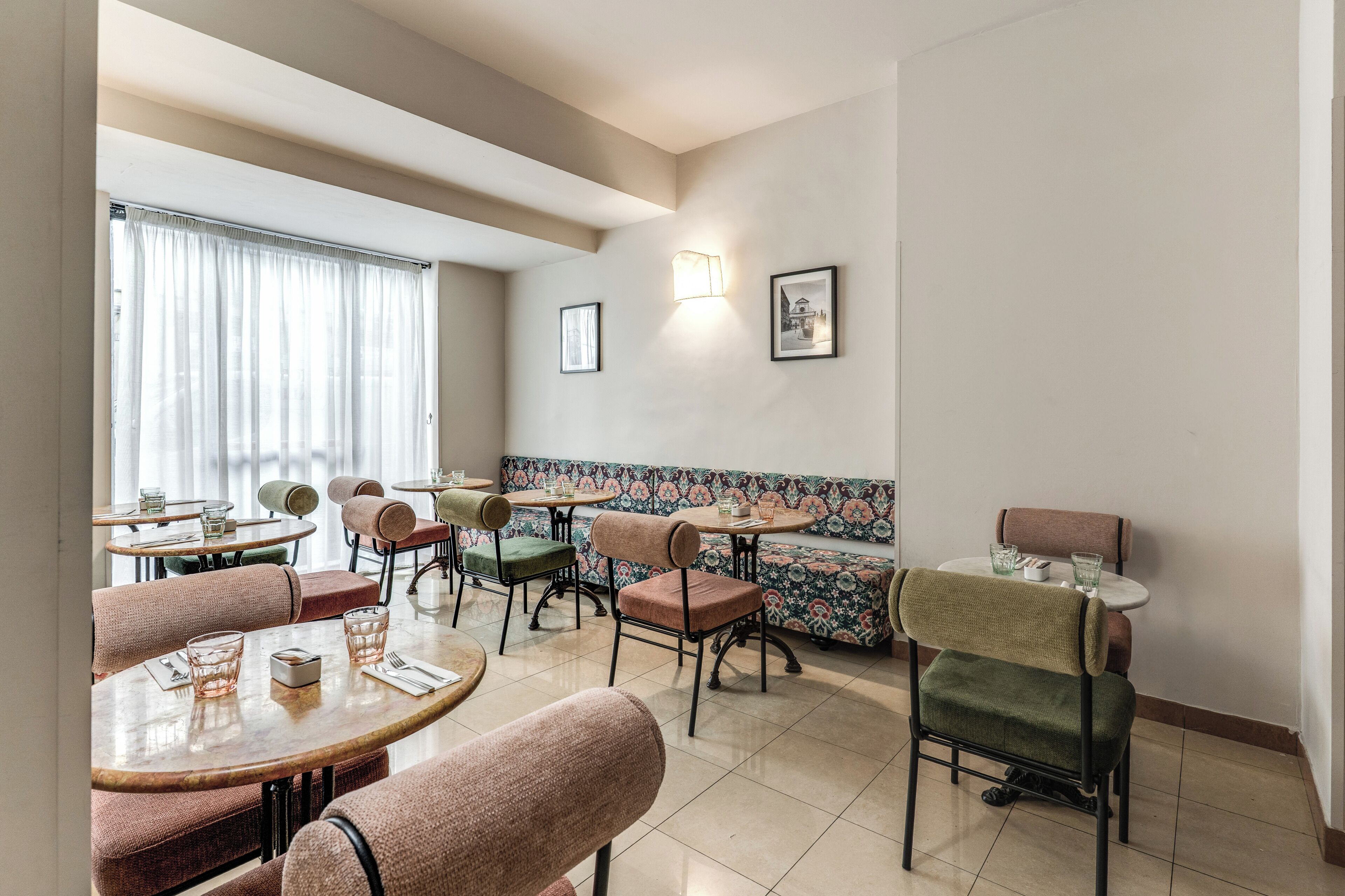 Un espace repas avec des tables rondes et des chaises rembourrées, un mur décoré de motifs et une fenêtre avec des rideaux.