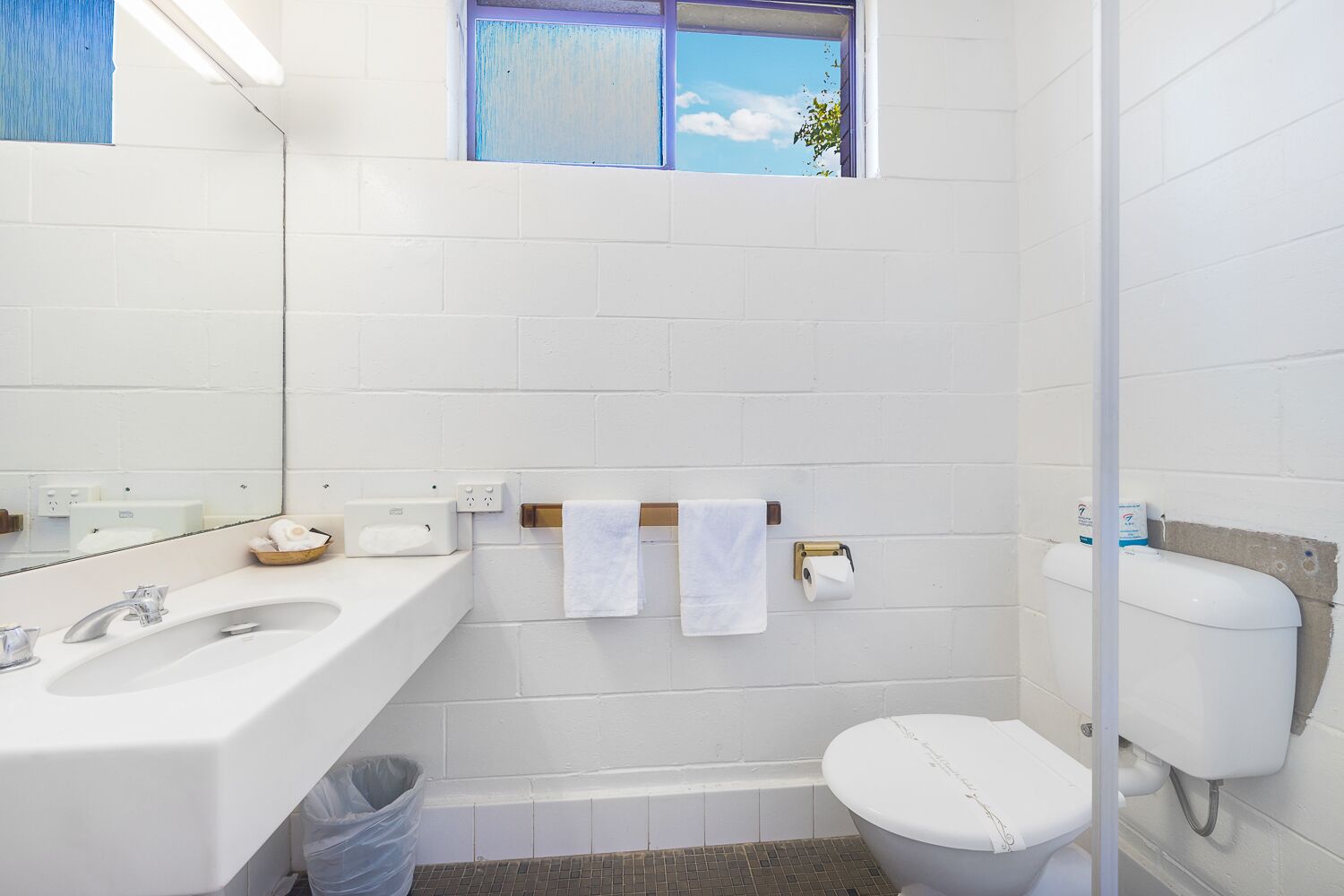 Une salle de bain avec des carreaux blancs, un lavabo, des toilettes, une fenêtre avec vue et un porte-serviettes.