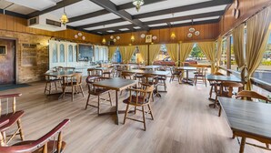 A restaurant with wooden furniture, a brick wall, and a view of the street. - Plainsman Motel (Forbes)