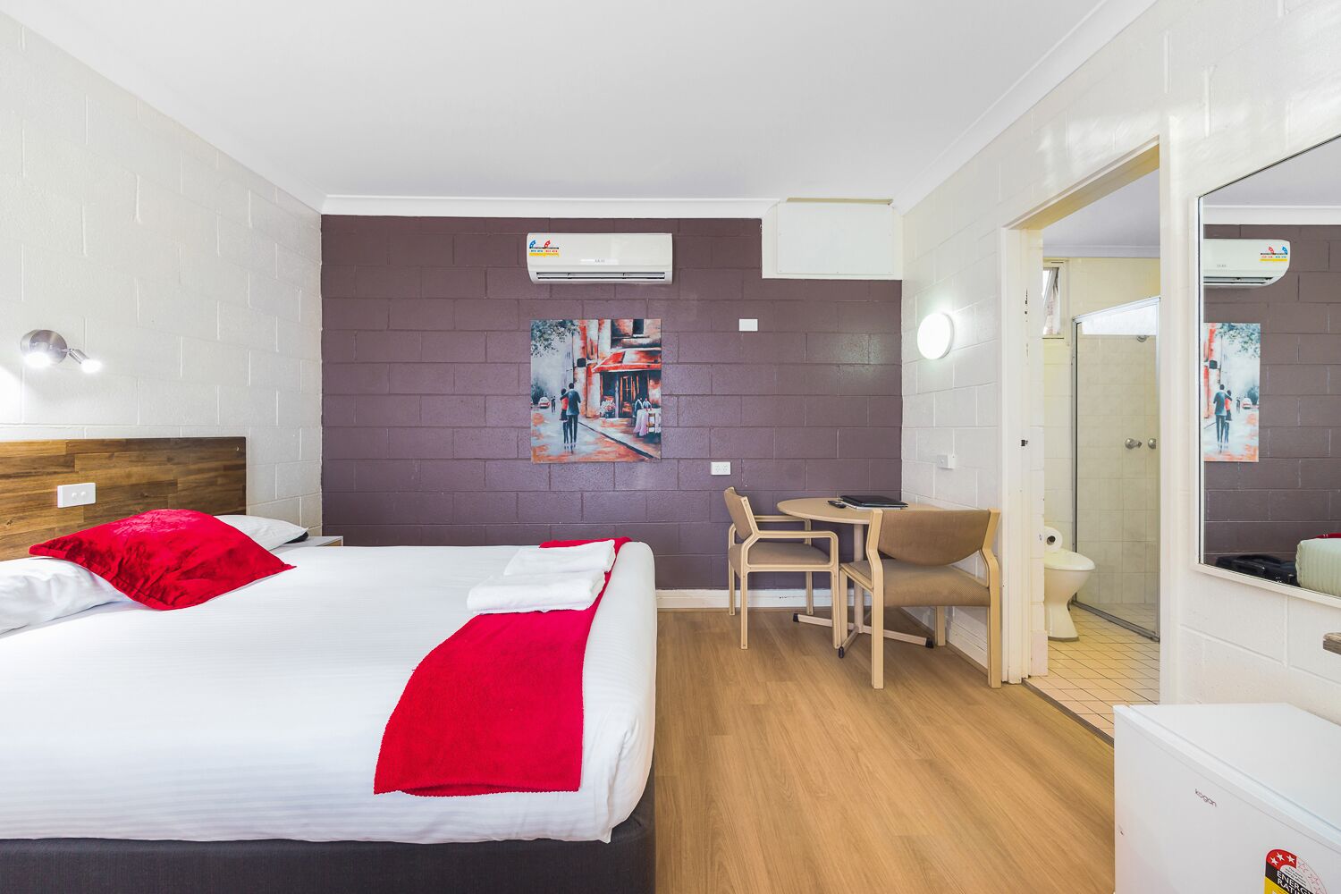 Habitación de hotel con cama, escritorio, silla, inodoro y zona de ducha.