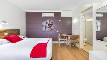 Habitación de hotel con cama, escritorio, silla, inodoro y zona de ducha.