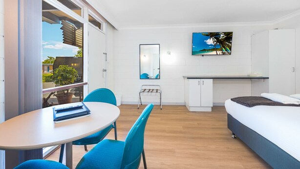 A modern room with a bed, a desk, a chair, and a small table. There is a window with blinds, a mirror, and a painting on the wall. - Plainsman Motel (Forbes)