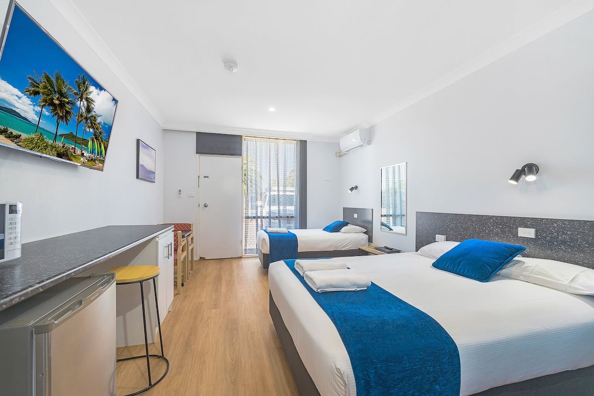 Quarto de hotel com duas camas, uma escrivaninha e vista para a praia pela janela.