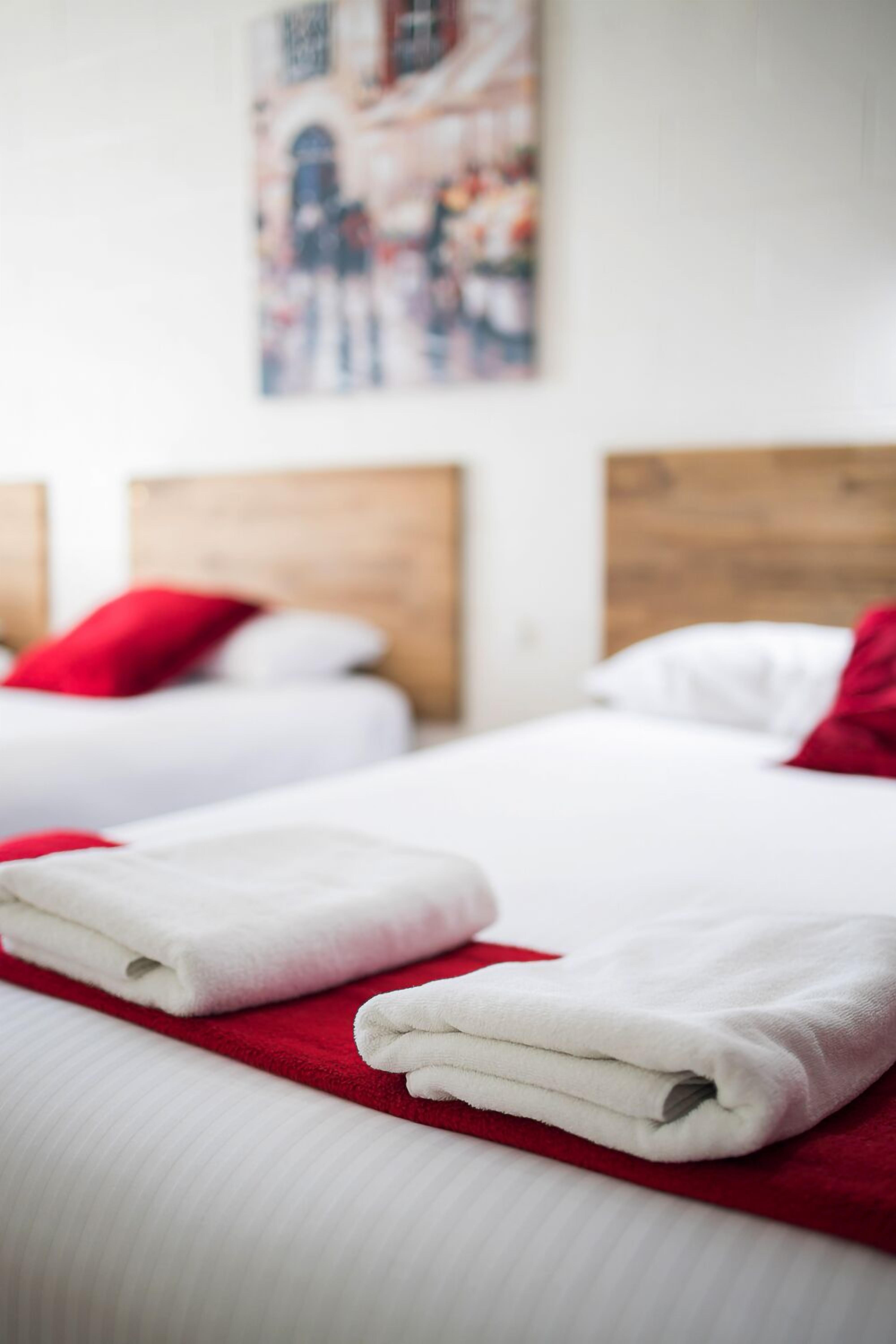 Quarto de hotel com duas camas, cada uma com cabeceira de madeira e almofadas vermelhas.