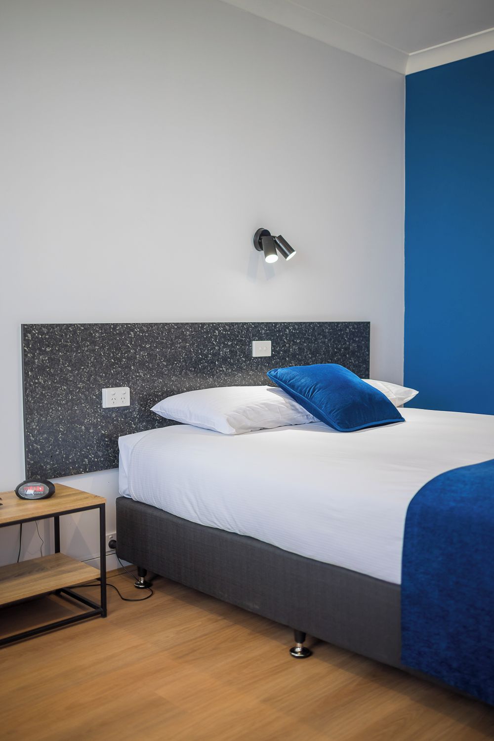 Una habitación de hotel moderna con una cama, una mesita de noche, una lámpara de pared y una pared de acento azul.