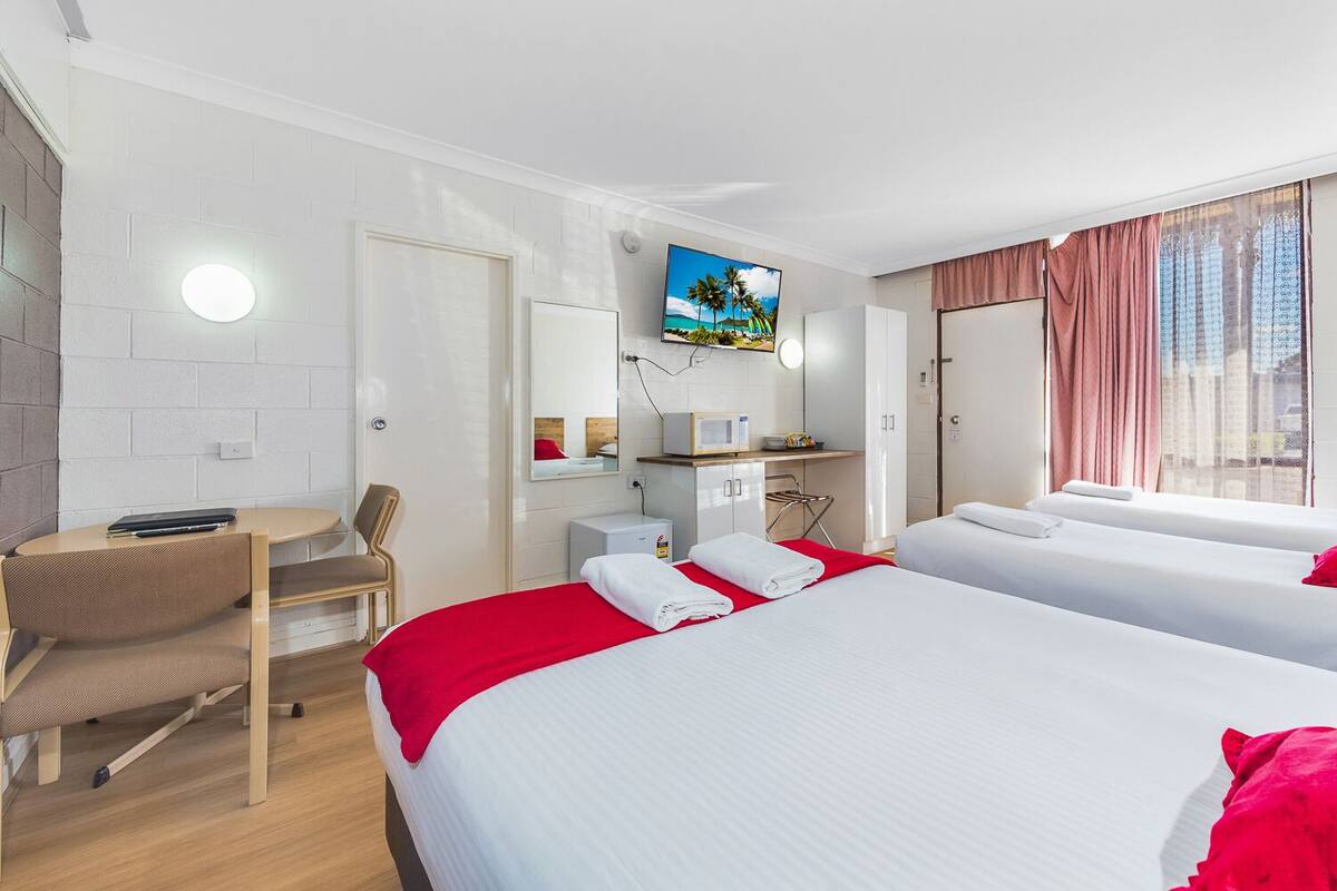 Quarto de hotel com duas camas, uma escrivaninha, uma cadeira, uma televisão e uma janela com cortinas.