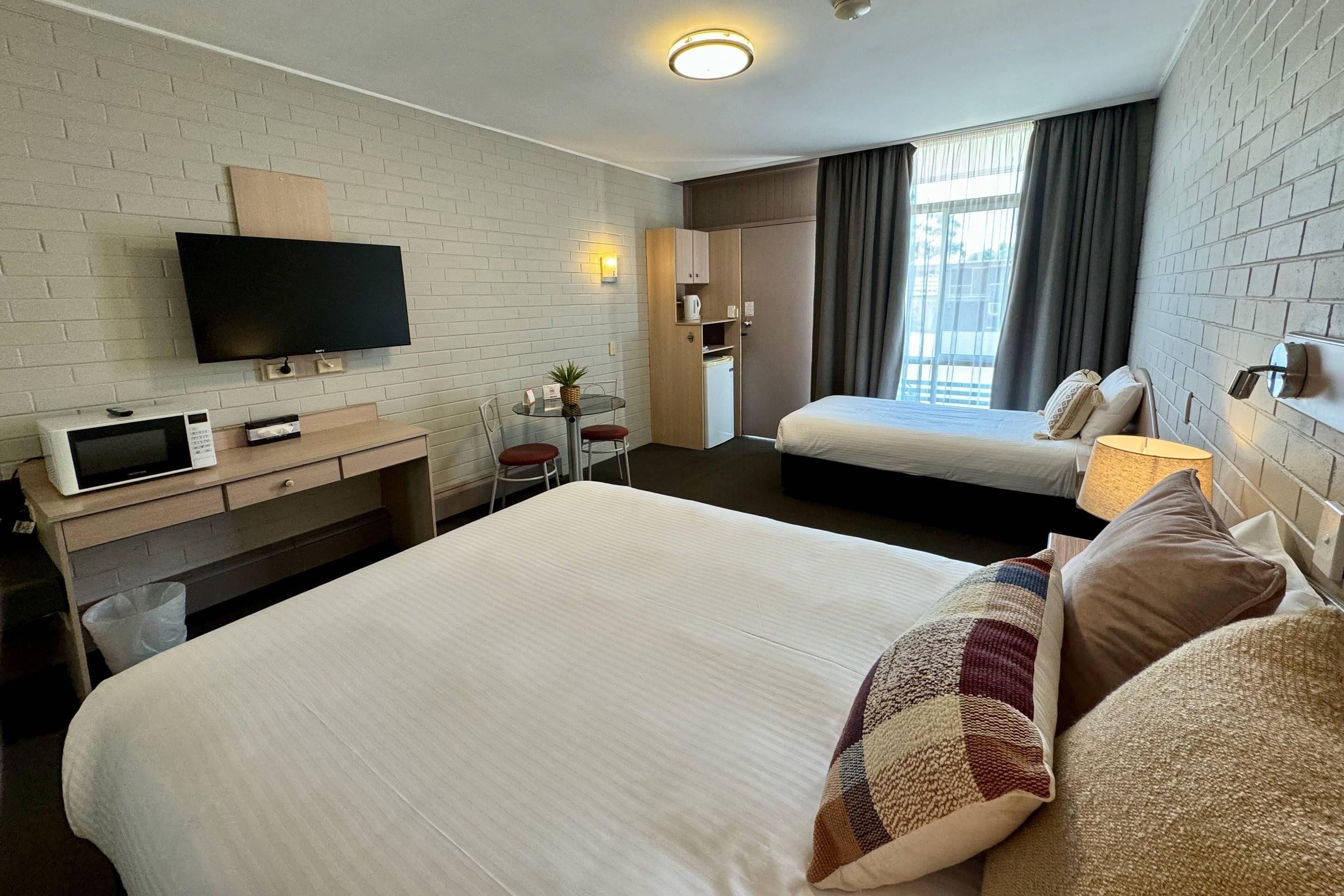Habitación de hotel con una cama grande, un televisor, un escritorio con computadora, una mesita con una planta y un armario.