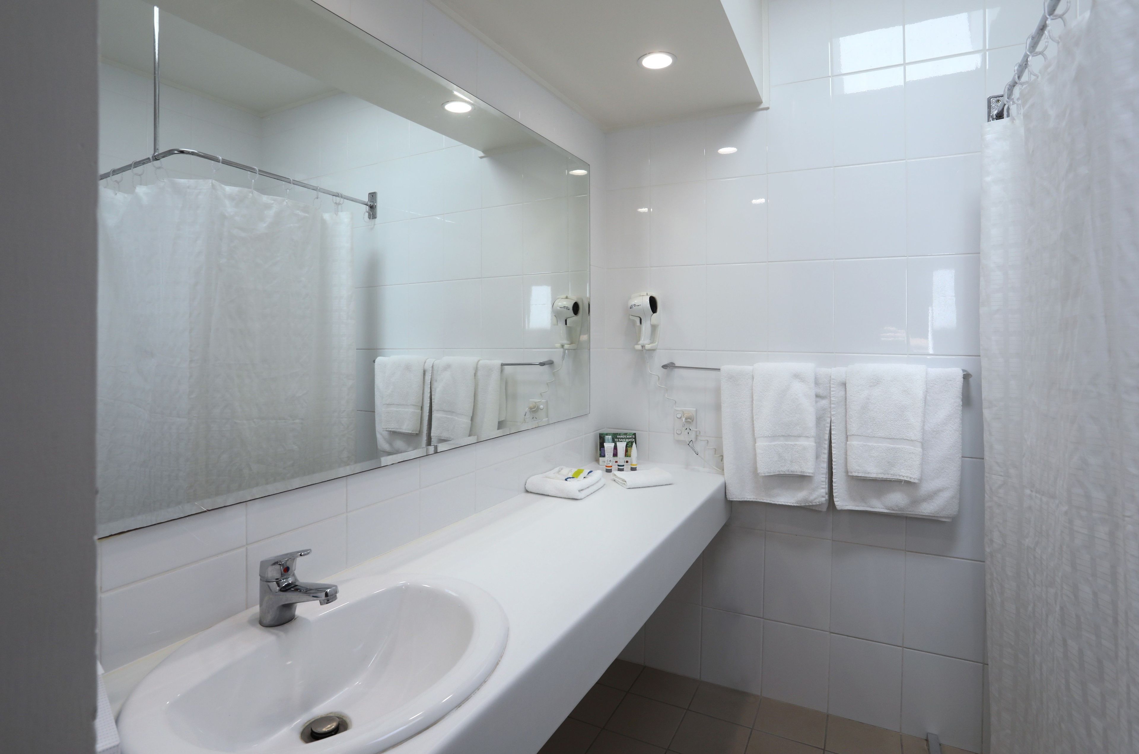 A modern bathroom with a large mirror, white sink, and towel rack.