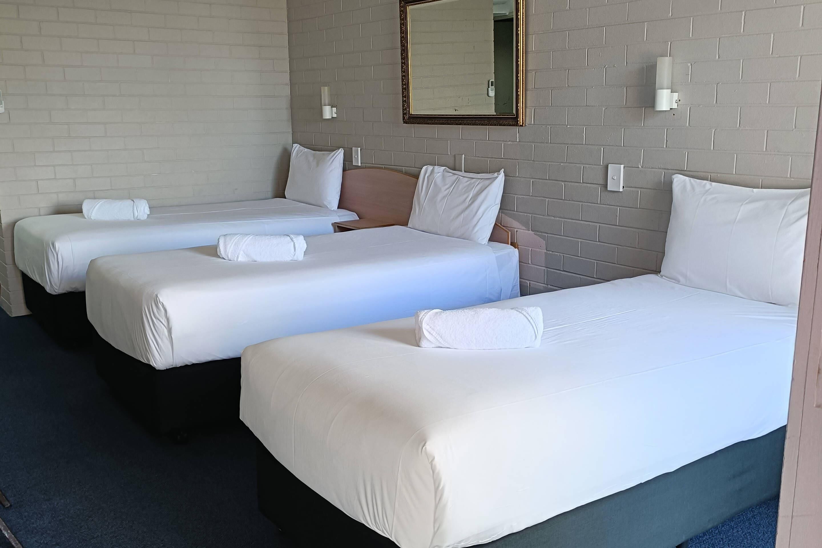 A hotel room with three single beds, a large mirror, and a brick wall.