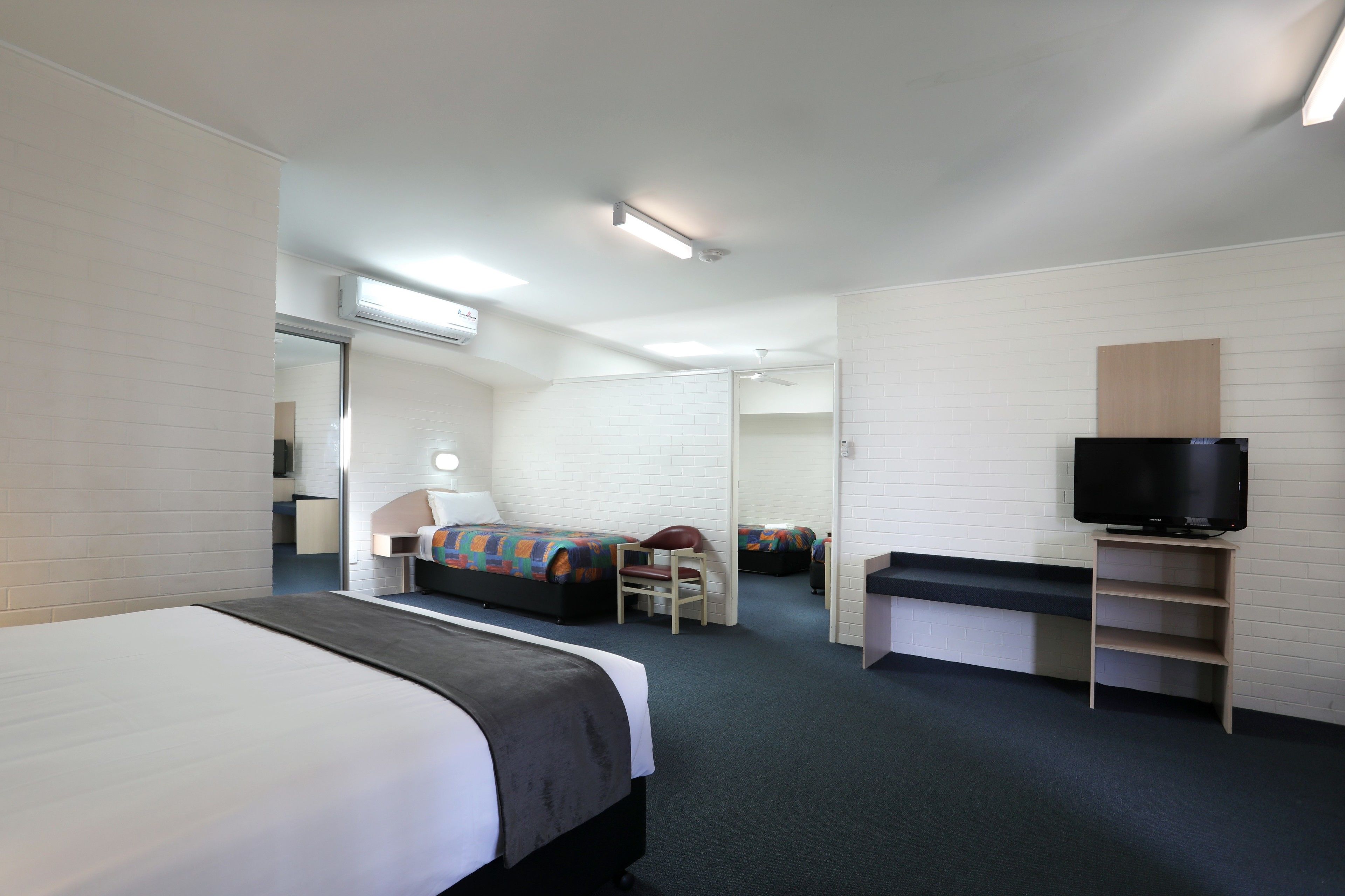 Habitación de hotel con cama, escritorio, silla, televisor y baño a la vista.