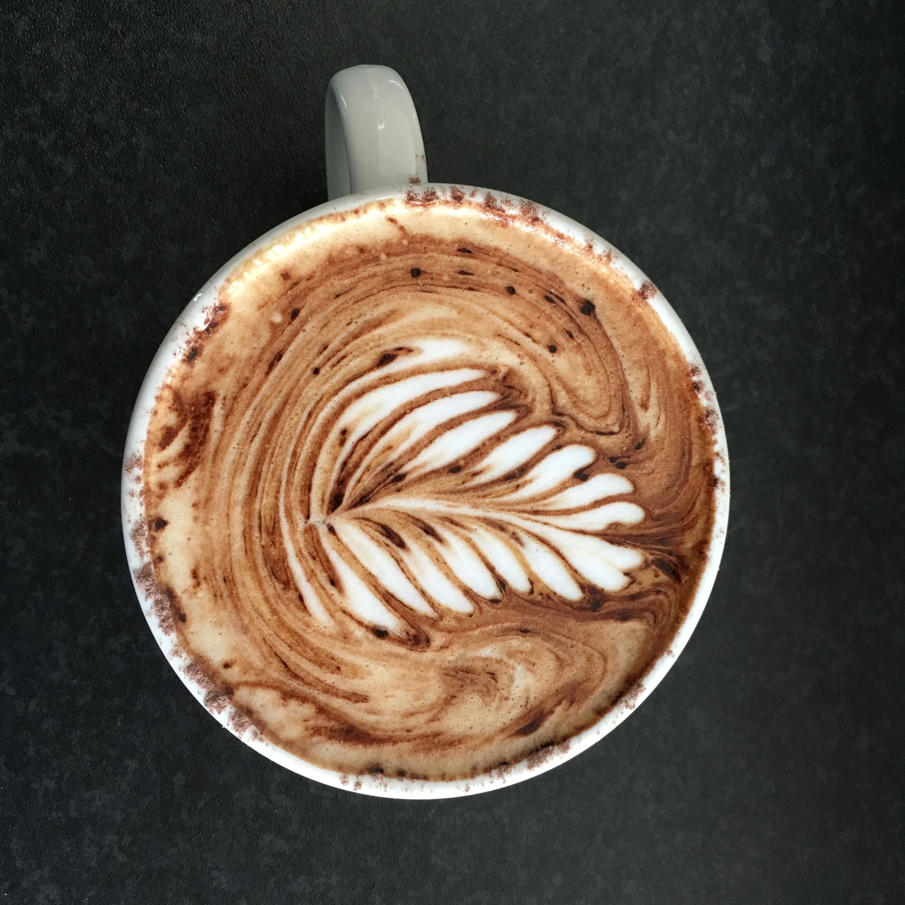 A cup of coffee with latte art on a dark surface.