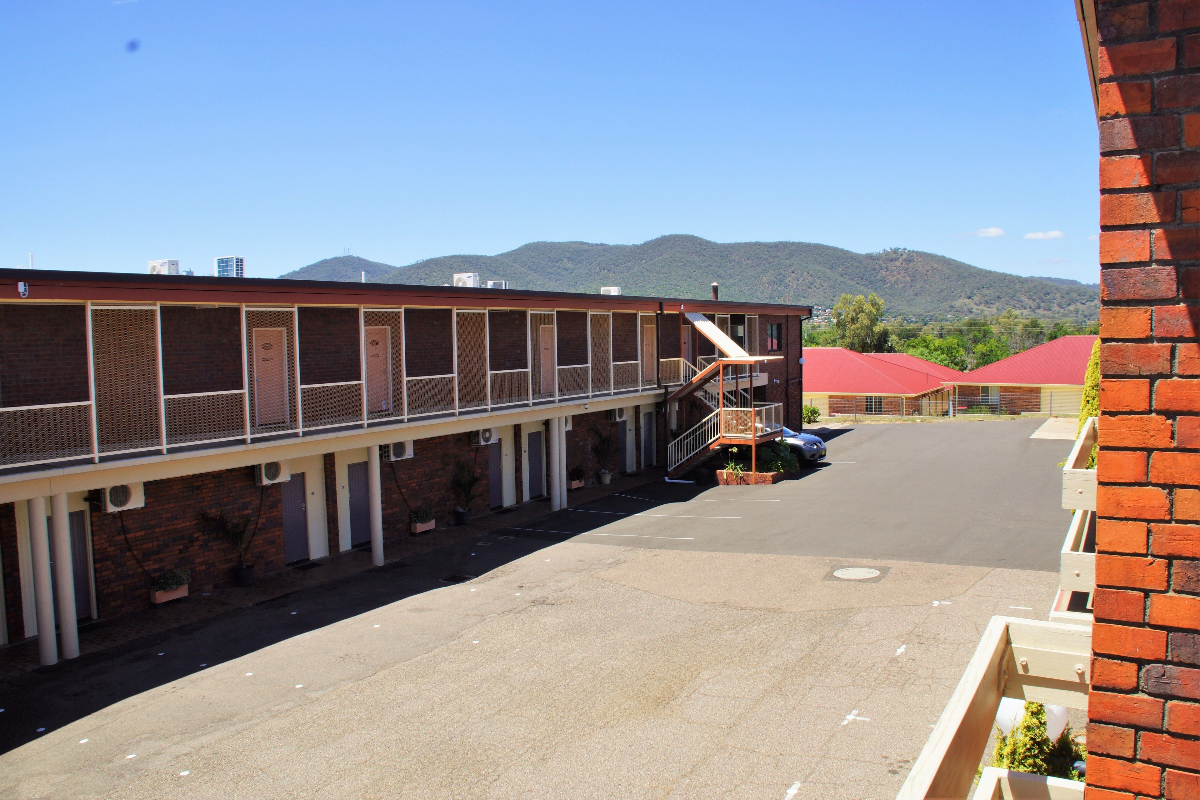 A motel with a long corridor of rooms, a central staircase, and a parking area.