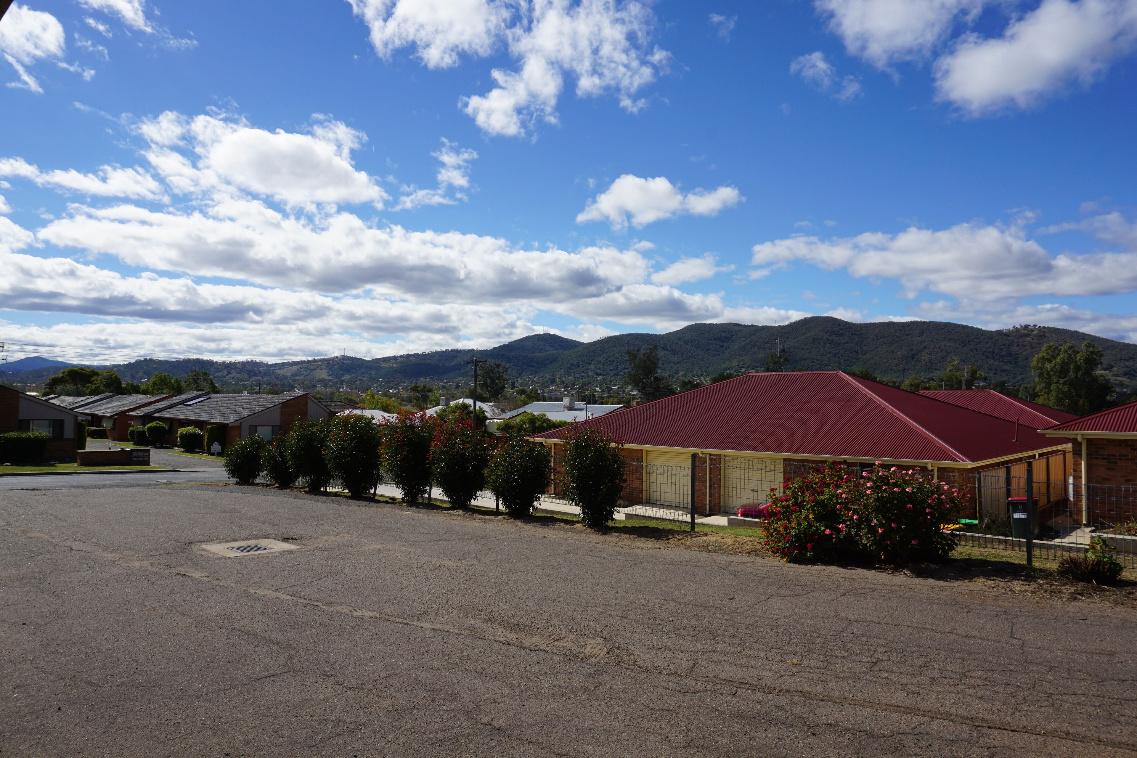 A row of single-story buildings with red roofs, a parking lot, and mountains in the background.