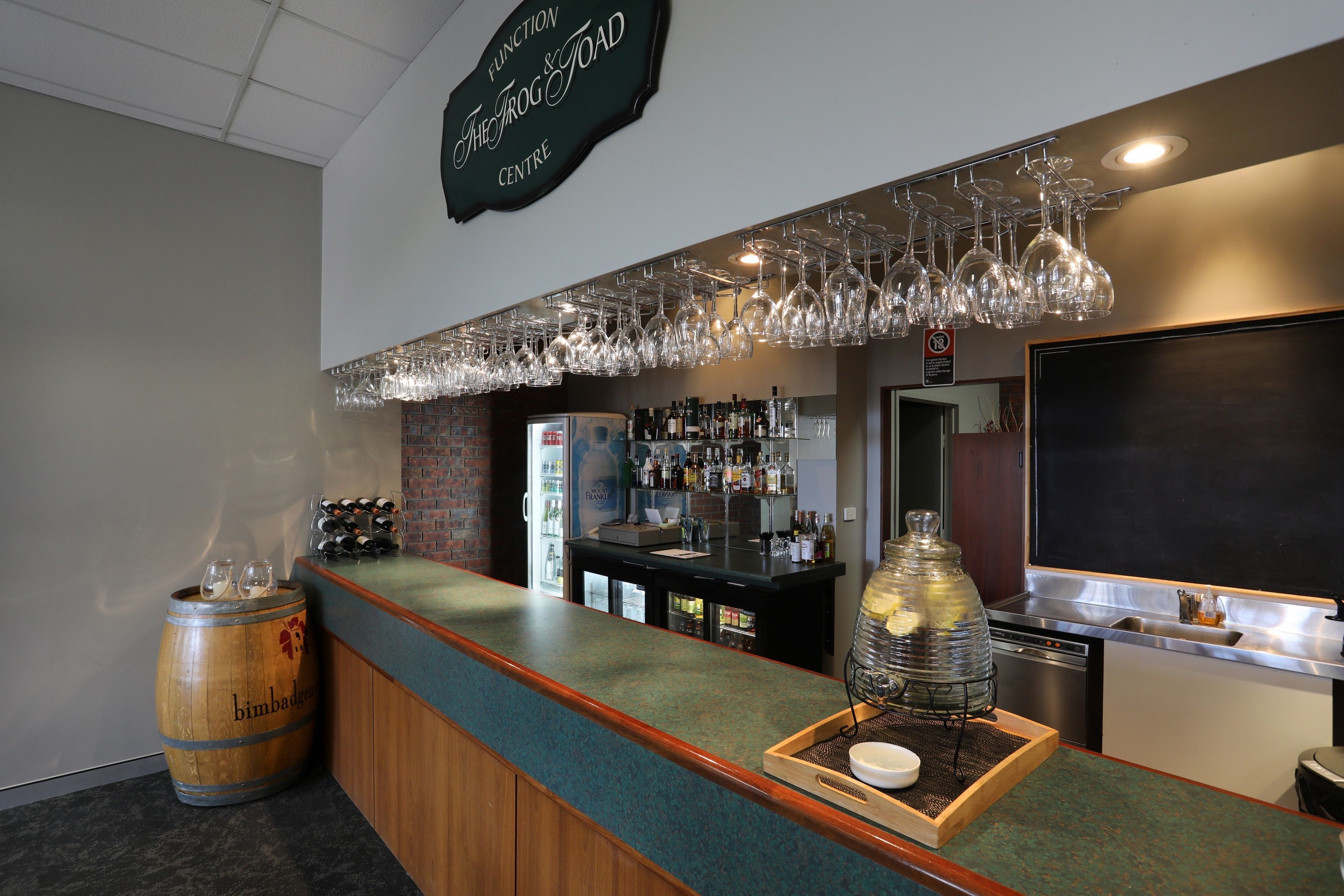 A bar area with a counter, wine glasses hanging above, a keg tap, and a chalkboard wall.