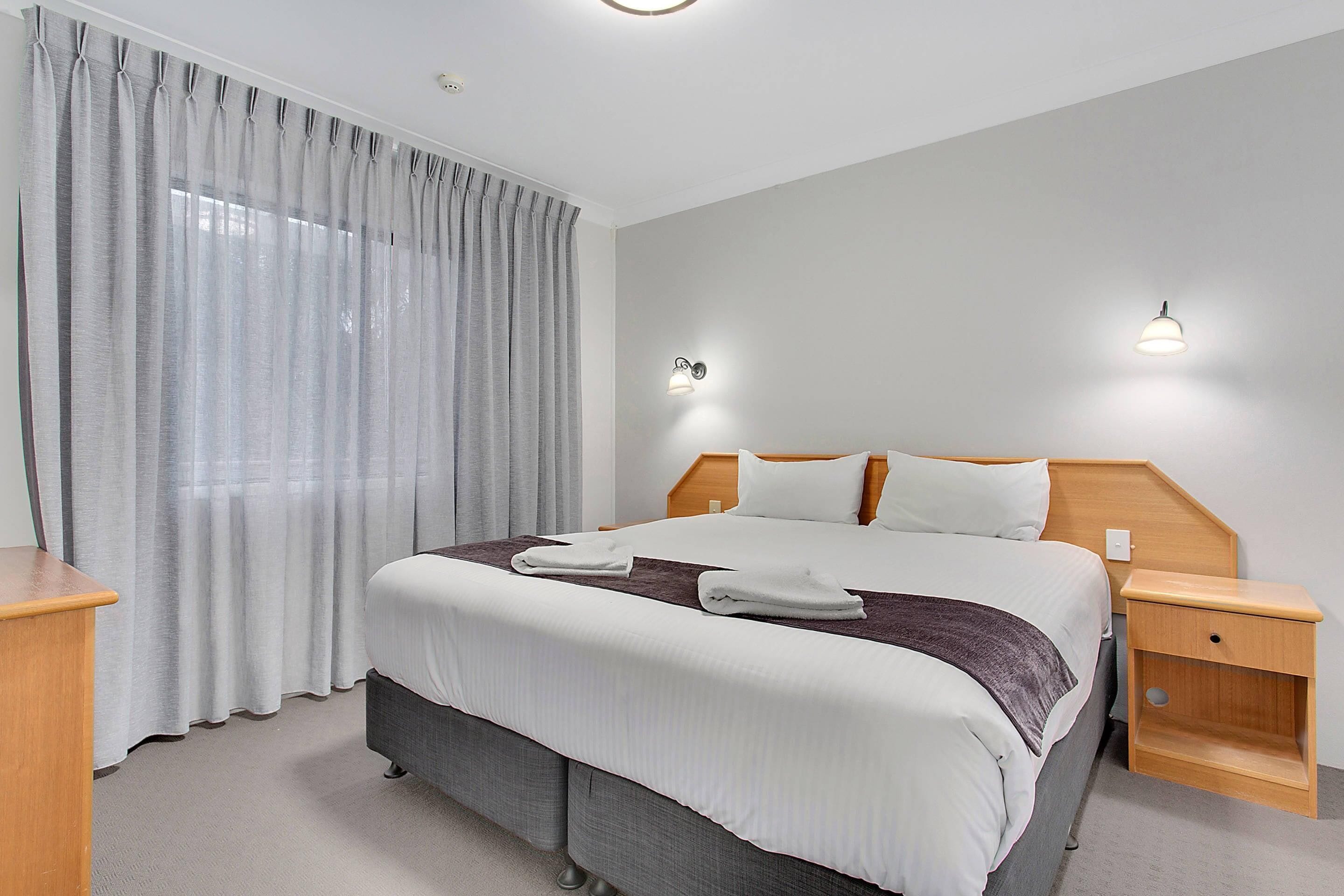A hotel room with a bed, a nightstand, a lamp, and a window with curtains.