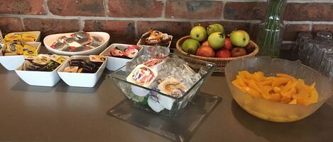 A buffet table with various food items, including fruits, cheeses, and packaged snacks.