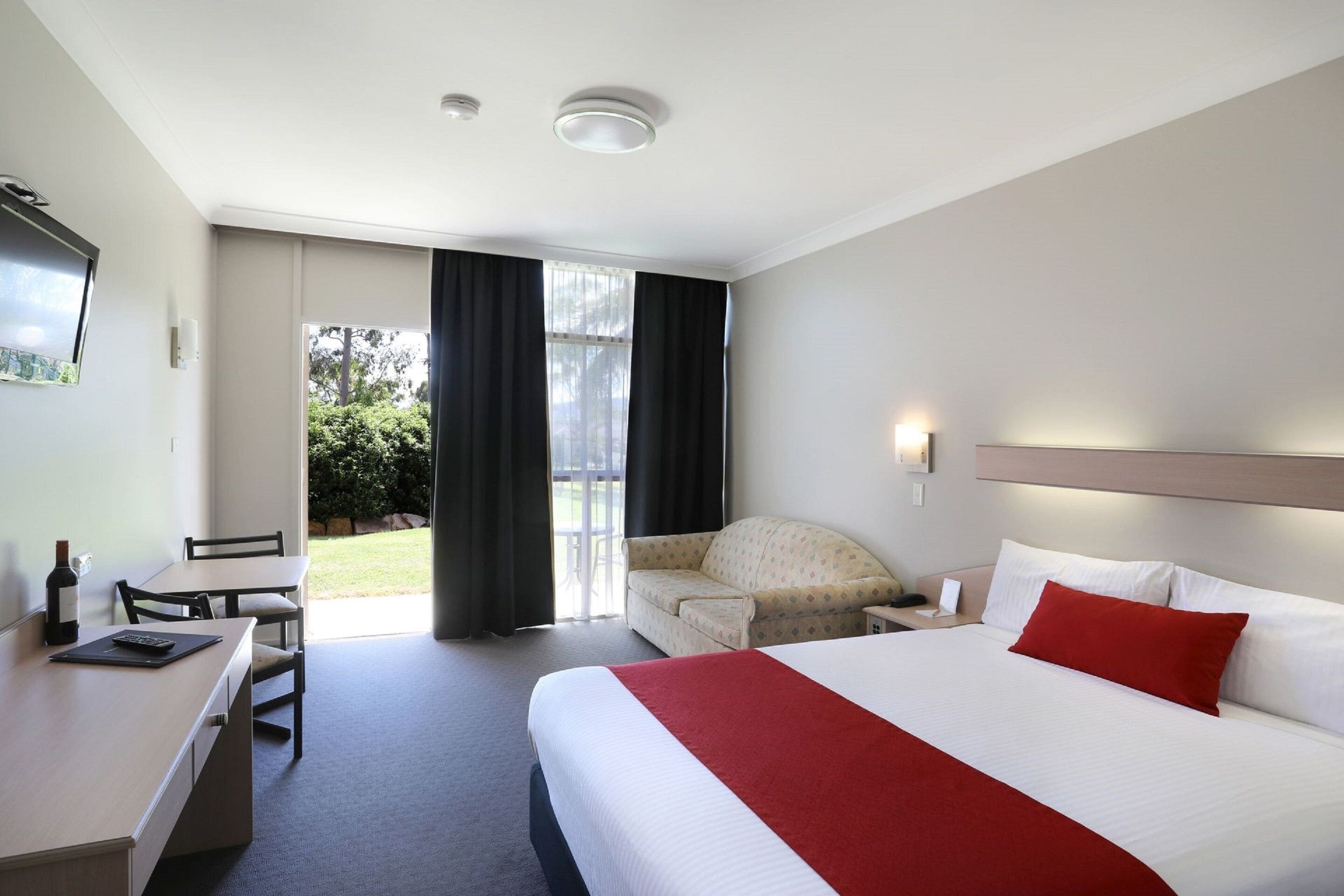 Una habitación de hotel con cama, escritorio, silla, sofá y ventana con cortinas.