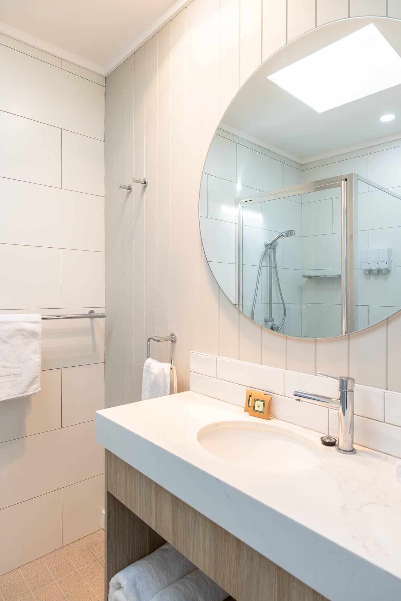 A modern bathroom with a round mirror, a sink with a faucet, and a shower area.