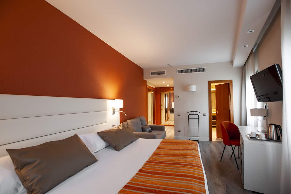 Une chambre d’hôtel avec un lit, un bureau, une chaise et un téléviseur.