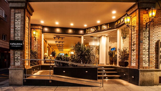 Hotellin sisäänkäynti, jossa portaat johtavat aulaan. Rakennuksessa on tiiliverhous, koristekasveja ruukuissa ja kyltti, jossa lukee: ”CATALONIA HOTEL”.