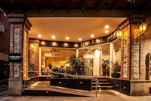 A hotel entrance with a staircase leading up to the lobby, featuring a brick facade, potted plants, and a sign that reads "CATALONIA HOTEL."