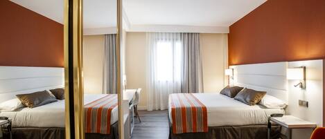 A hotel room with two beds, a desk, and a chair.