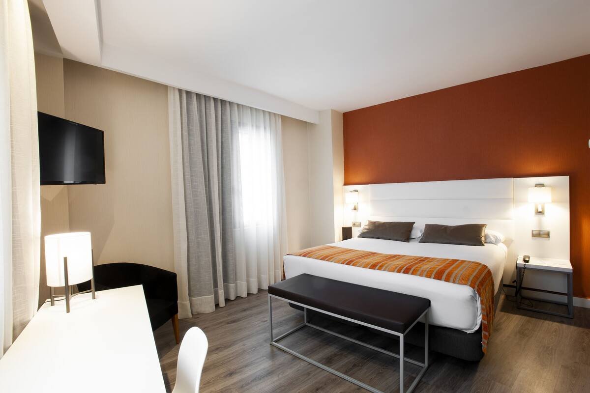 Une chambre d’hôtel comprenant un lit, des tables de chevet, un bureau, une chaise, une télévision et des rideaux.