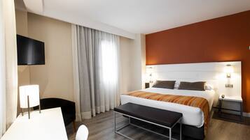 A hotel room with a bed, bedside tables, a desk, a chair, a TV, and curtains.