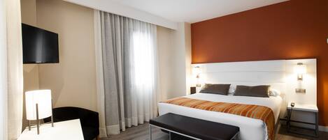 A hotel room with a bed, bedside tables, a desk, a chair, a TV, and curtains.