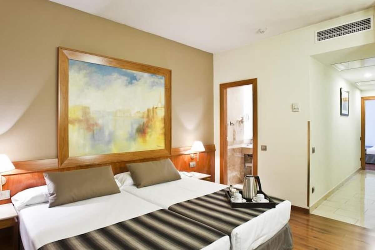 A hotel room with a bed, two bedside tables, a painting, a coffee maker, and a view of a hallway.