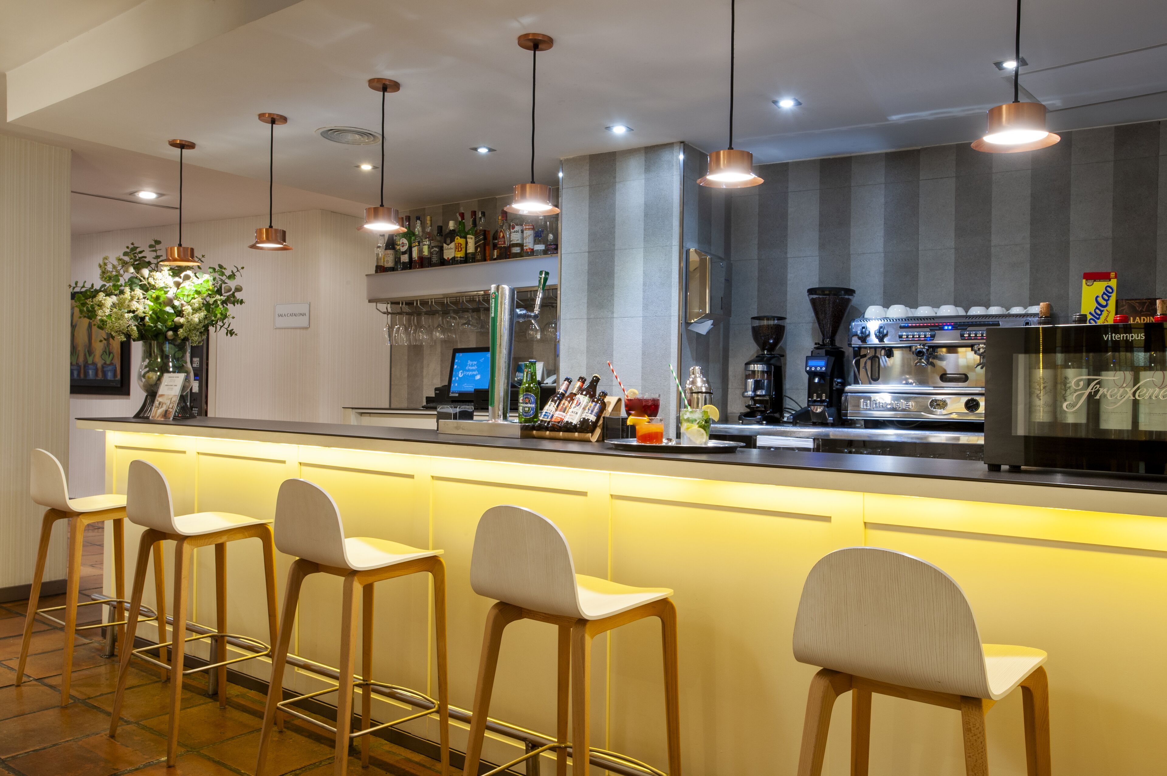 Eine Bar mit einer langen Theke, mehreren Barhocker und Deckenleuchten.