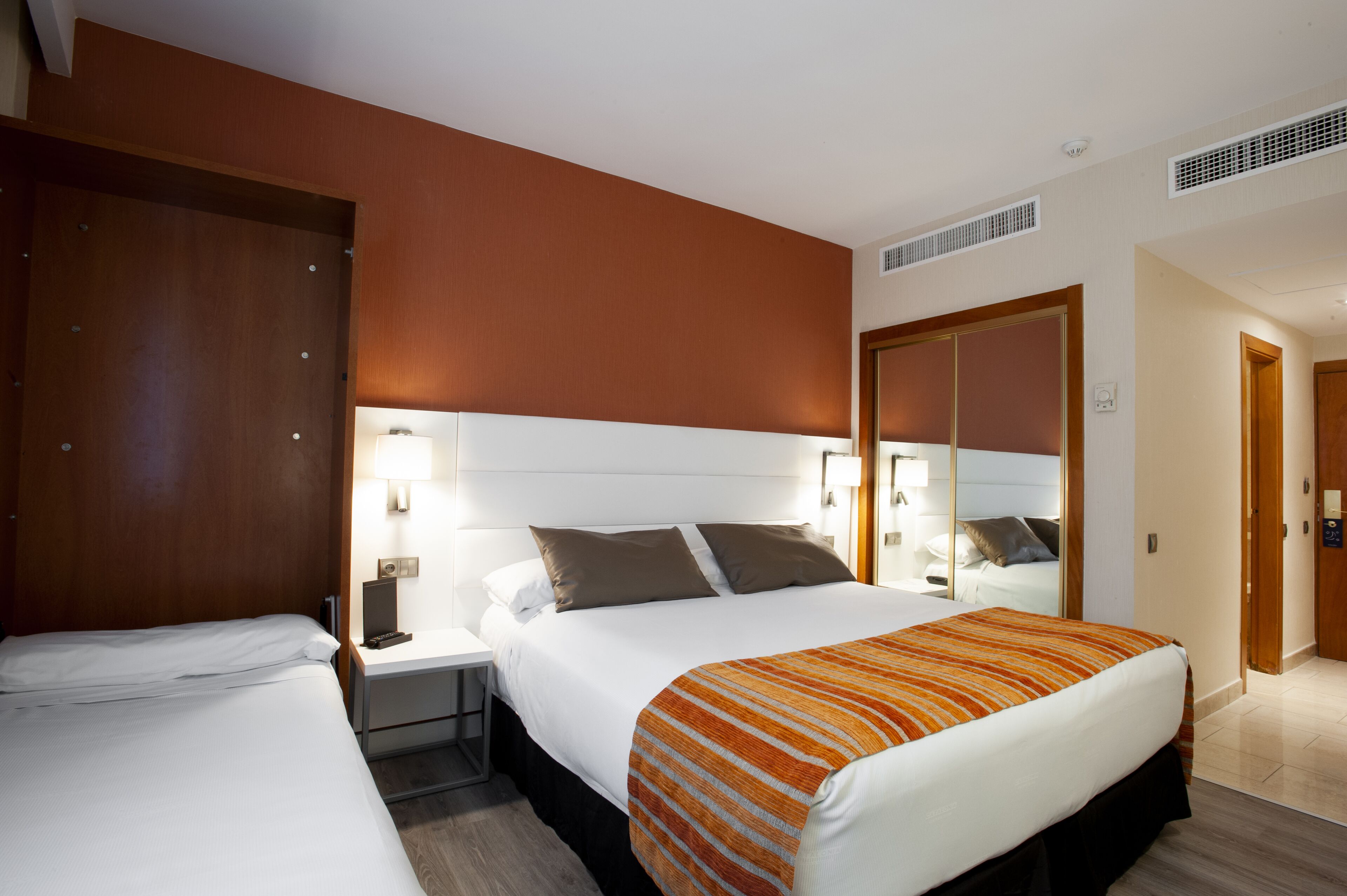 A hotel room with two beds, a large mirror, and a nightstand with a lamp.
