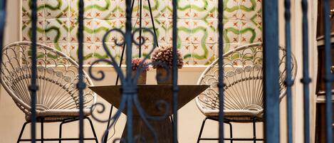 Un comedor con una mesa redonda, dos sillas de mimbre, un florero con flores y una pared decorada al fondo.