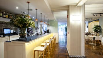 Een moderne bar met een lange toonbank, meerdere barkrukken en diverse flessen op planken.