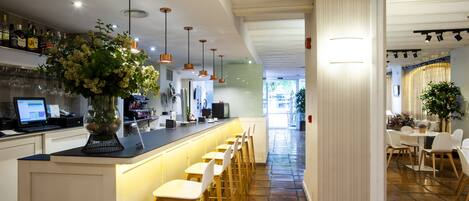 A modern bar area with a long counter, multiple bar stools, and a variety of bottles on shelves.