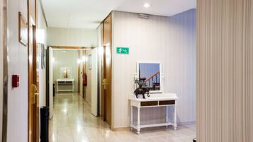 A hotel hallway with a reception desk, a fire extinguisher, and an emergency exit sign.