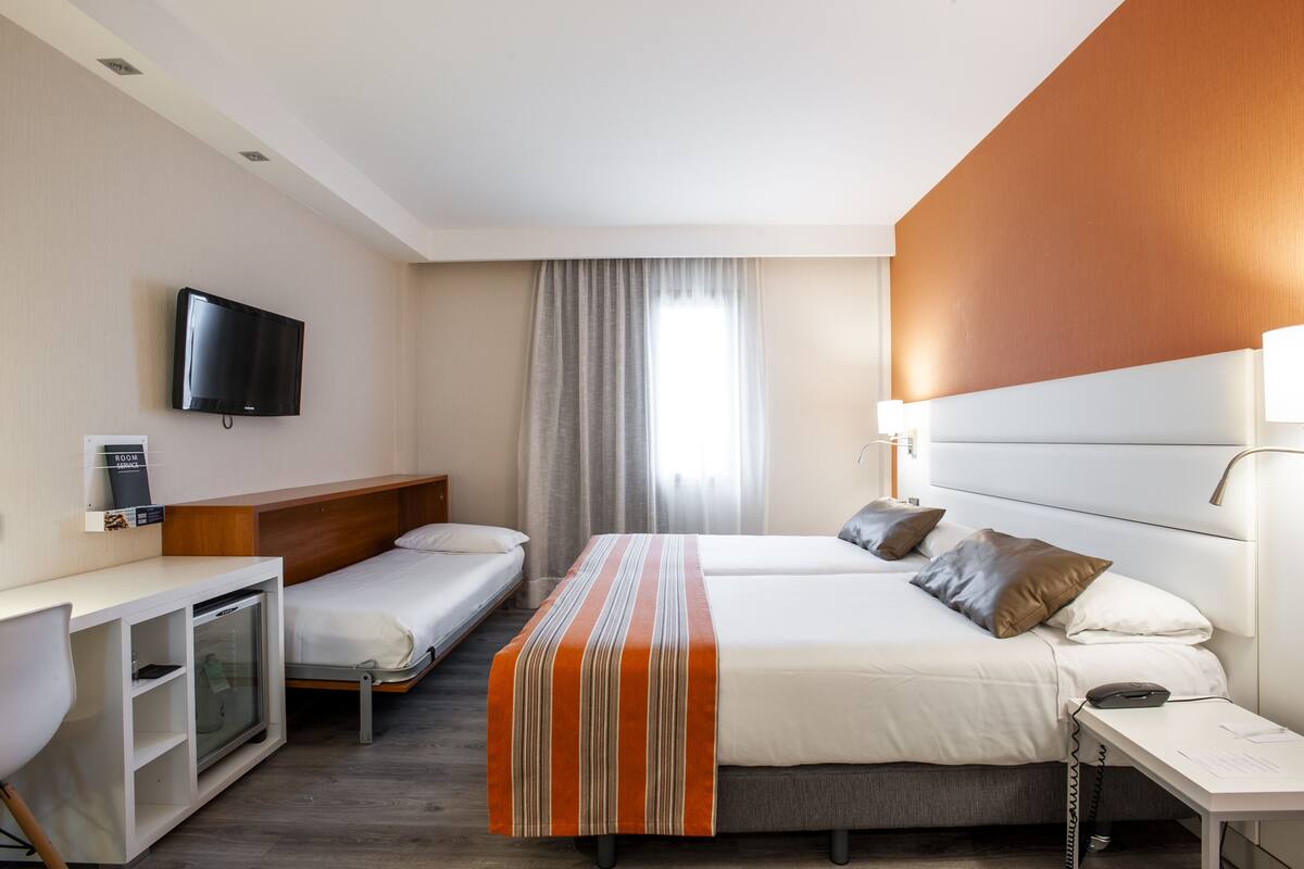 Une chambre d’hôtel avec un lit, un bureau, une télévision et une fenêtre avec des rideaux.