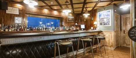 A bar area with a long counter, multiple stools, and a variety of bottles.