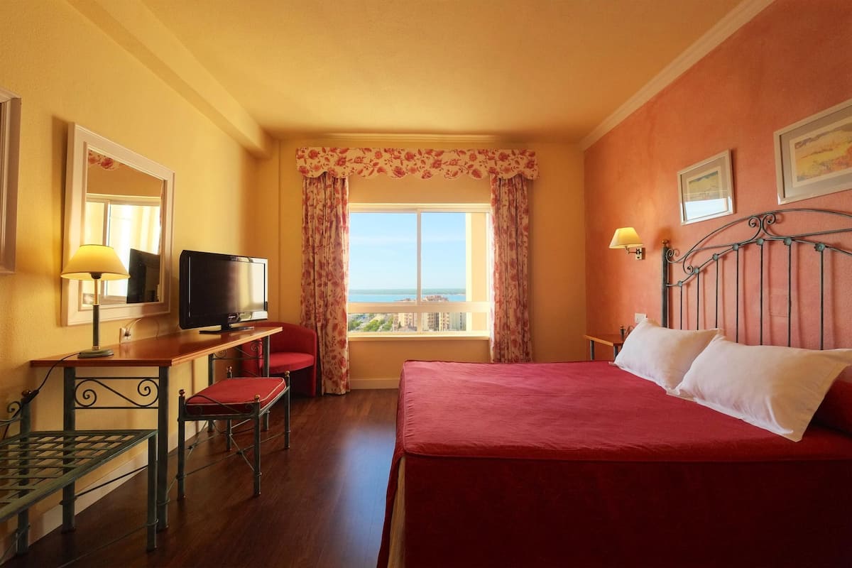 Een hotelkamer met een bed, een bureau met televisie, een stoel en een raam met gordijnen.