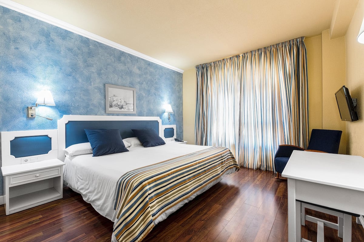 Een hotelkamer met een bed, nachtkastjes, een bureau, een stoel, een televisie en een raam met gordijnen.