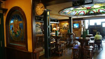A bar with wooden stools, a clock, and a stained glass window.