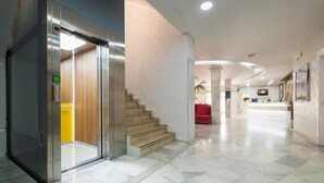 A modern hotel lobby with a marble floor, a reception desk, a staircase, and a red seating area.
