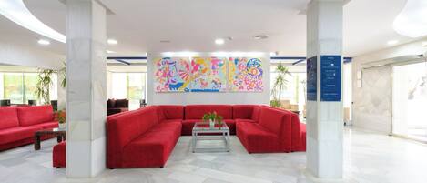 A spacious lobby with a large red sectional sofa, a glass coffee table, and a colorful abstract mural on the wall.