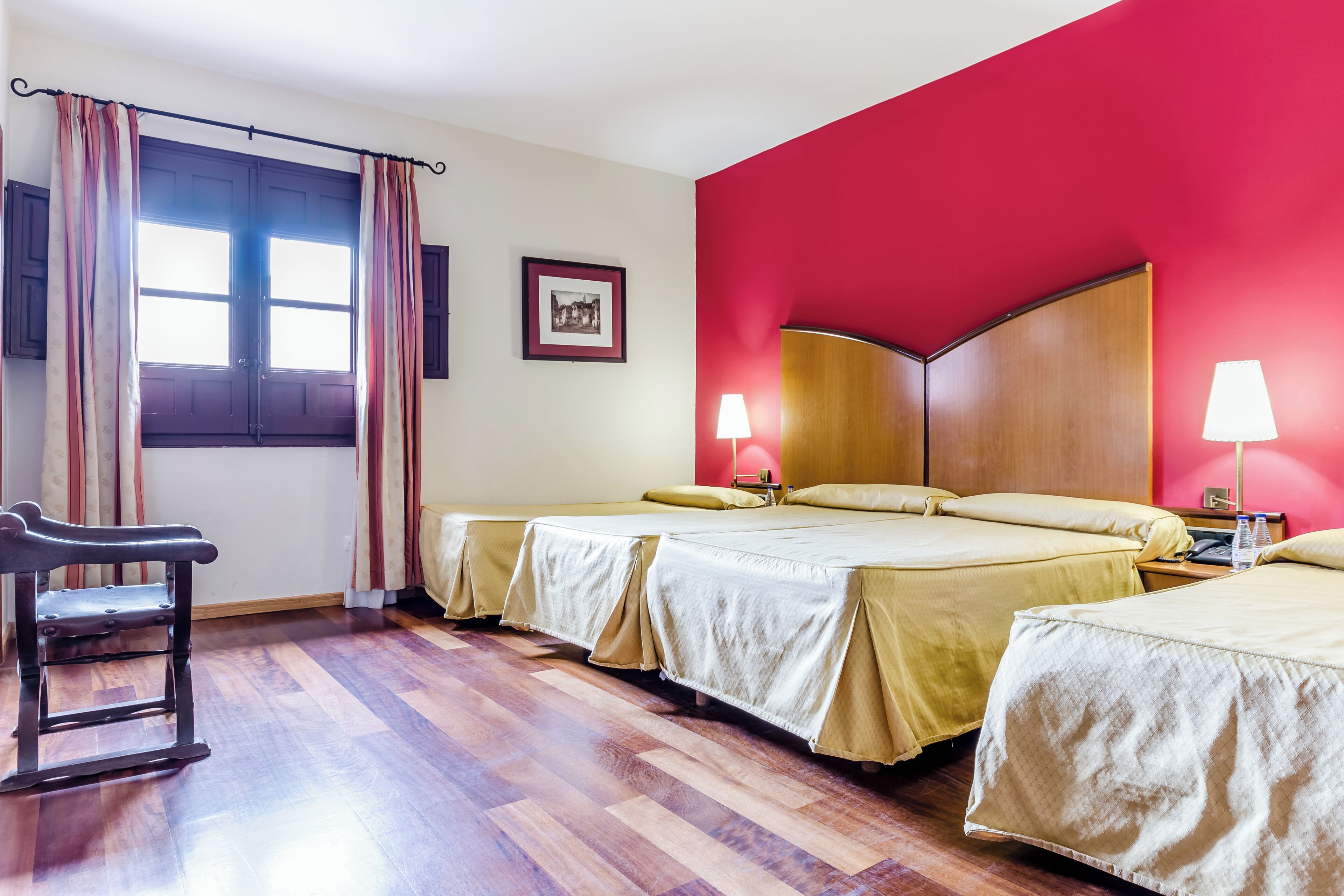 Habitación de hotel con dos camas, cabecera de madera, una silla y una ventana con cortinas.